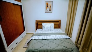 A bedroom with a bed, a wooden headboard, a wardrobe, and a painting on the wall. - Juru House Rentals  (Kigali)