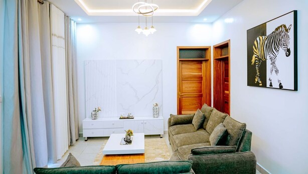 A modern living room with a sofa, coffee table, and artwork on the wall. - Juru House Rentals  (Kigali)