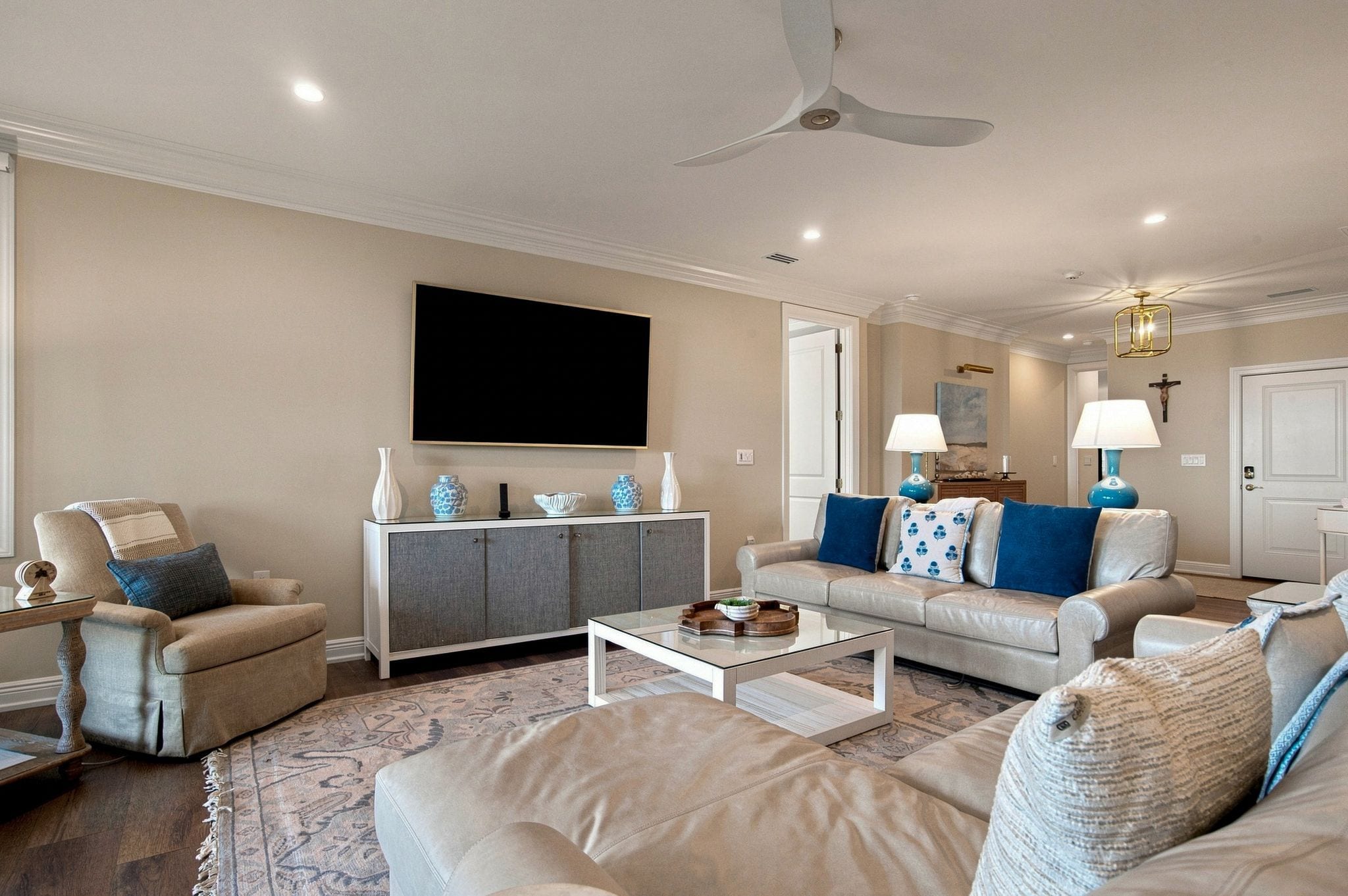 A living room with a sofa, armchairs, a coffee table, a TV, and a ceiling fan.