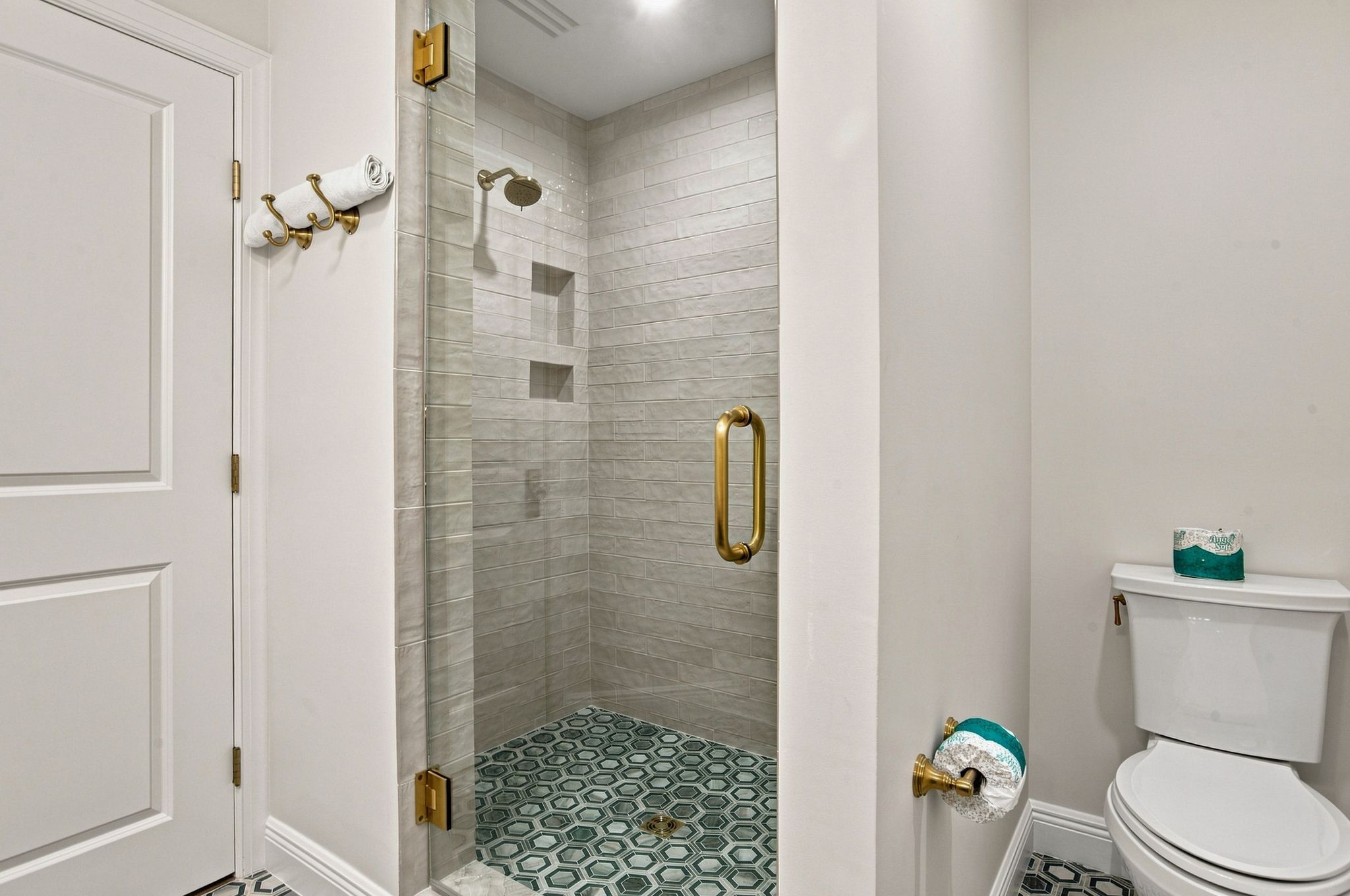 A bathroom with a shower, toilet, and a door with a towel rack.