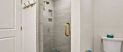 A bathroom with a shower, toilet, and a door with a towel rack.