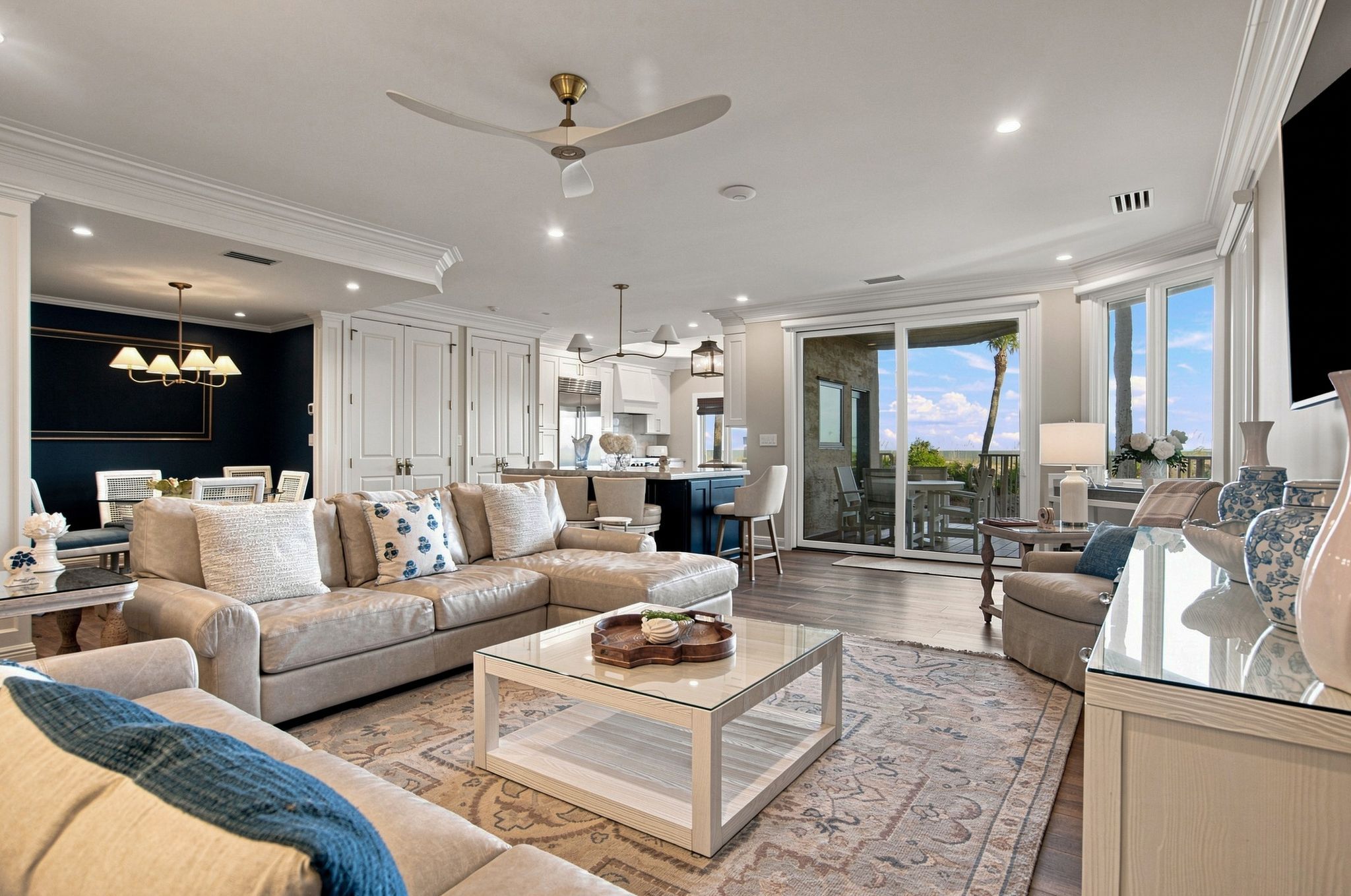 A spacious living room with a large sofa, a coffee table, and a view of the kitchen and balcony.