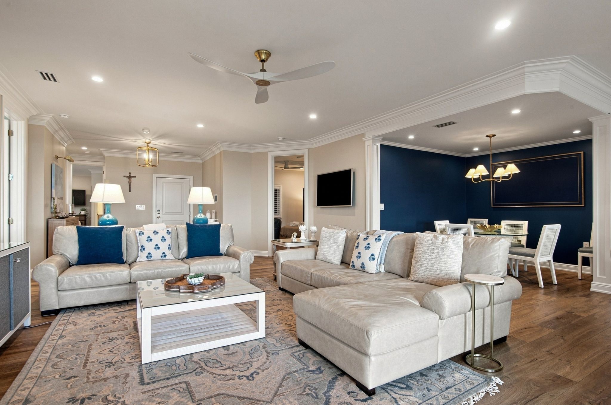 A spacious living room with a large sectional sofa, a coffee table, and a television mounted on the wall.