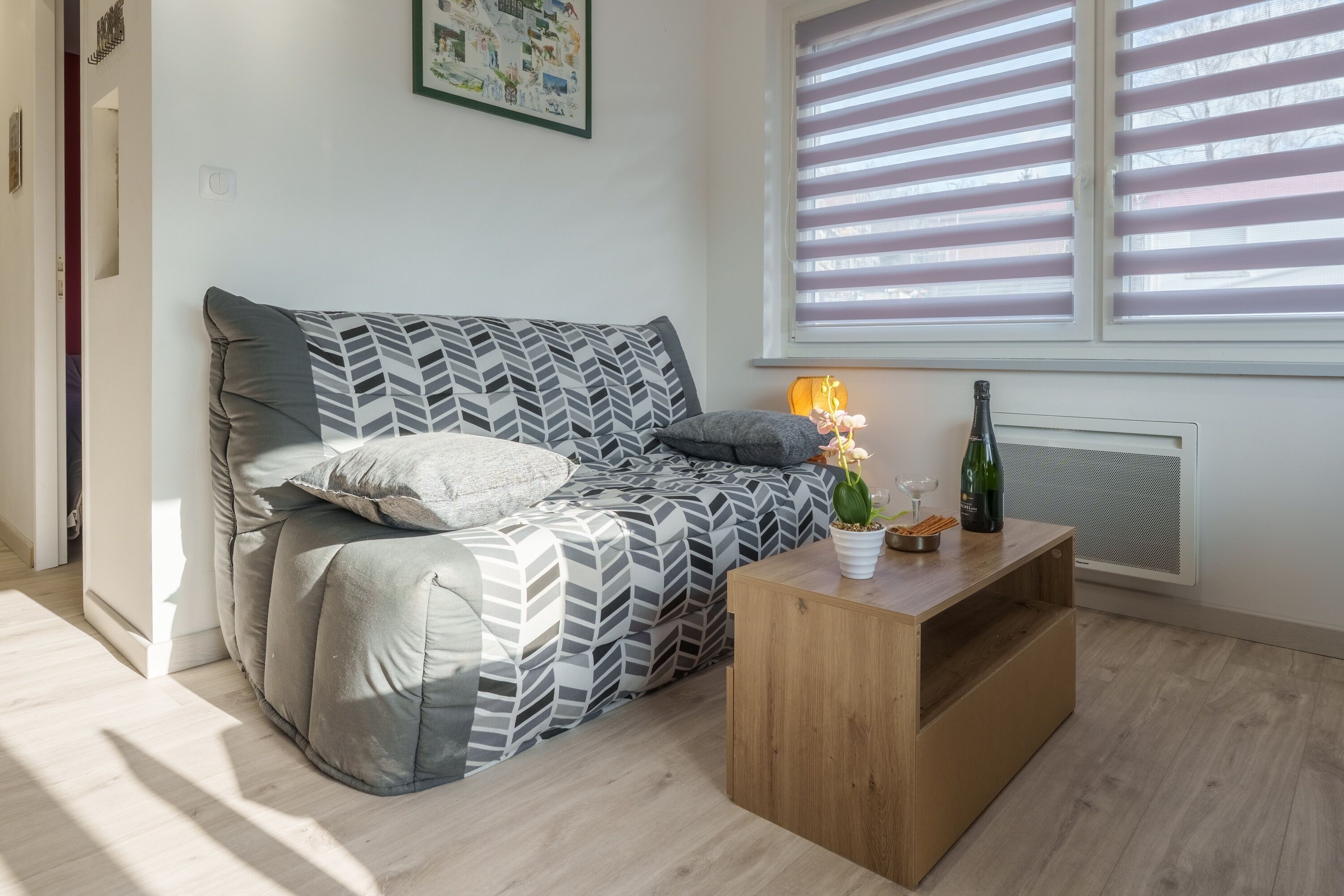 En moderne stue med sofa, sofabord i træ og et vindue med persienner.