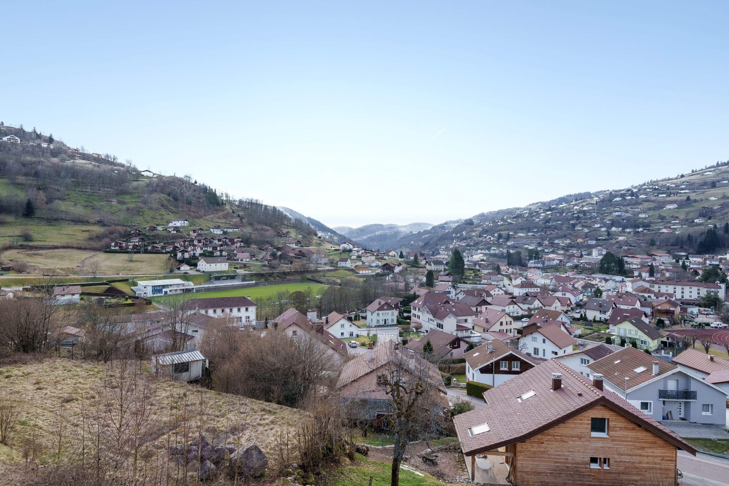 Un quartier résidentiel avec des maisons, dont certaines ont des toits inclinés, et un paysage vallonné en arrière-plan.