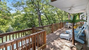 Une terrasse en bois avec une rambarde, des meubles d’extérieur et une vue sur une zone boisée.
