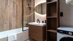 Ein modernes Badezimmer mit Waschtisch aus Holz, einer integrierten Waschmaschine und einem großen Spiegel.