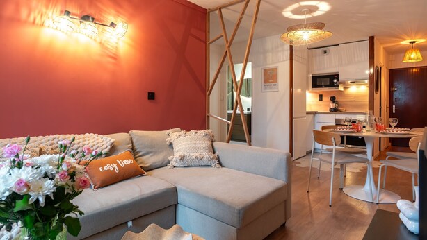 Ein modernes Wohnzimmer mit einer Eckcouch, einem Essbereich mit Tisch und Stühlen, einer Küche mit Mikrowelle und einer Treppe.