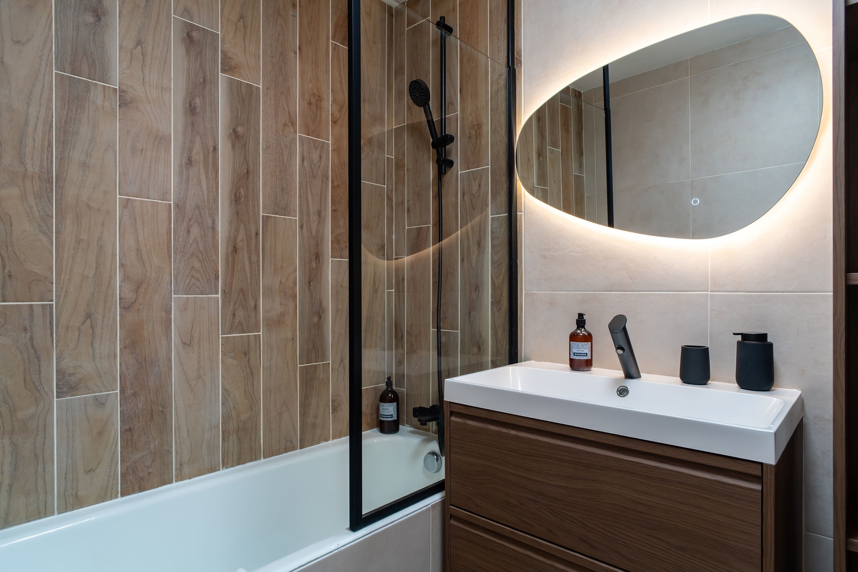 A modern bathroom with a wooden wall, a white bathtub, a mirror, and a vanity with a sink.