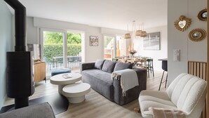 A modern living room with a sofa, a white armchair, a round coffee table, a fireplace, and a dining area with chairs and a table. - La Perle d'Arzon - Maison familiale en bord de mer (Arzon)