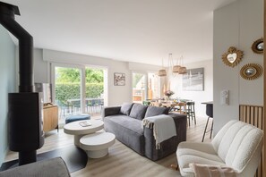 Una sala de estar moderna con un sofá, un sillón blanco, una mesa de centro redonda, una chimenea y un comedor con sillas y una mesa.
