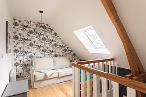 A loft bedroom with a sloped ceiling, a white sofa, a wooden staircase, and a skylight. - La Perle d'Arzon - Maison familiale en bord de mer (Arzon)