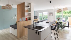 A modern kitchen with a central island, wooden cabinets, and a dining area with chairs and a table. - La Perle d'Arzon - Maison familiale en bord de mer (Arzon)