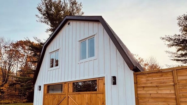 A white barn with two large wooden doors and a wooden fence. - Private Barn Loft w/ King Bed | Cozy Forest Escape (Parry Sound)