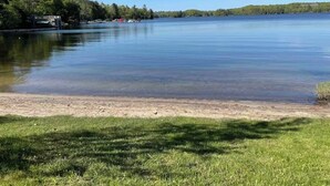 A calm lake with a grassy shoreline, trees in the background, and a clear sky. - Private Barn Loft w/ King Bed | Cozy Forest Escape (Parry Sound)