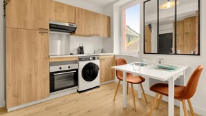 Cozinha compacta com armários de madeira, forno embutido, máquina de lavar e área de refeições com mesa e cadeiras.