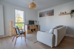 Ein modernes Wohnzimmer mit einer Couch, einem Korbstuhl, einem Fernseher auf einem Holzboden und einem großen Fenster.