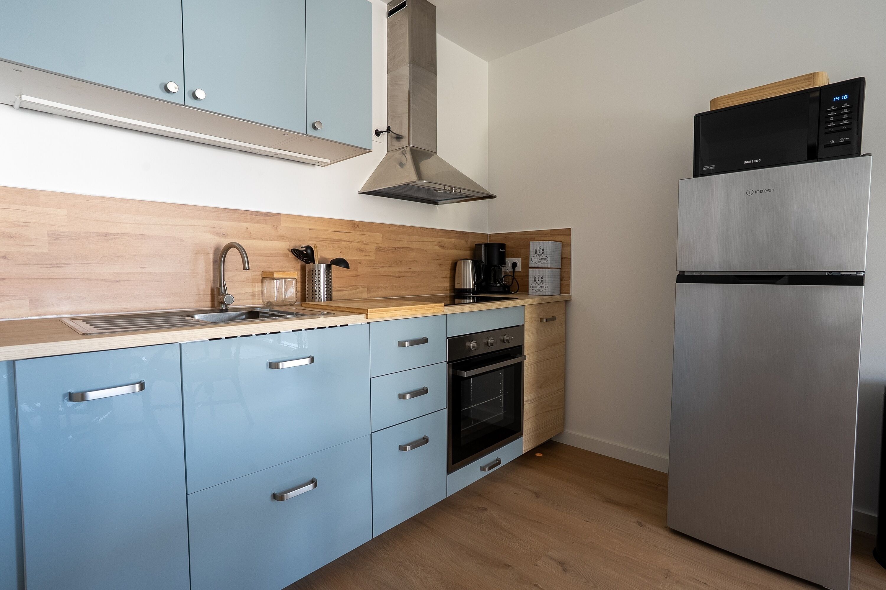 A modern kitchen with light blue cabinets, a stainless steel range hood, a microwave, a coffee maker, and a refrigerator.