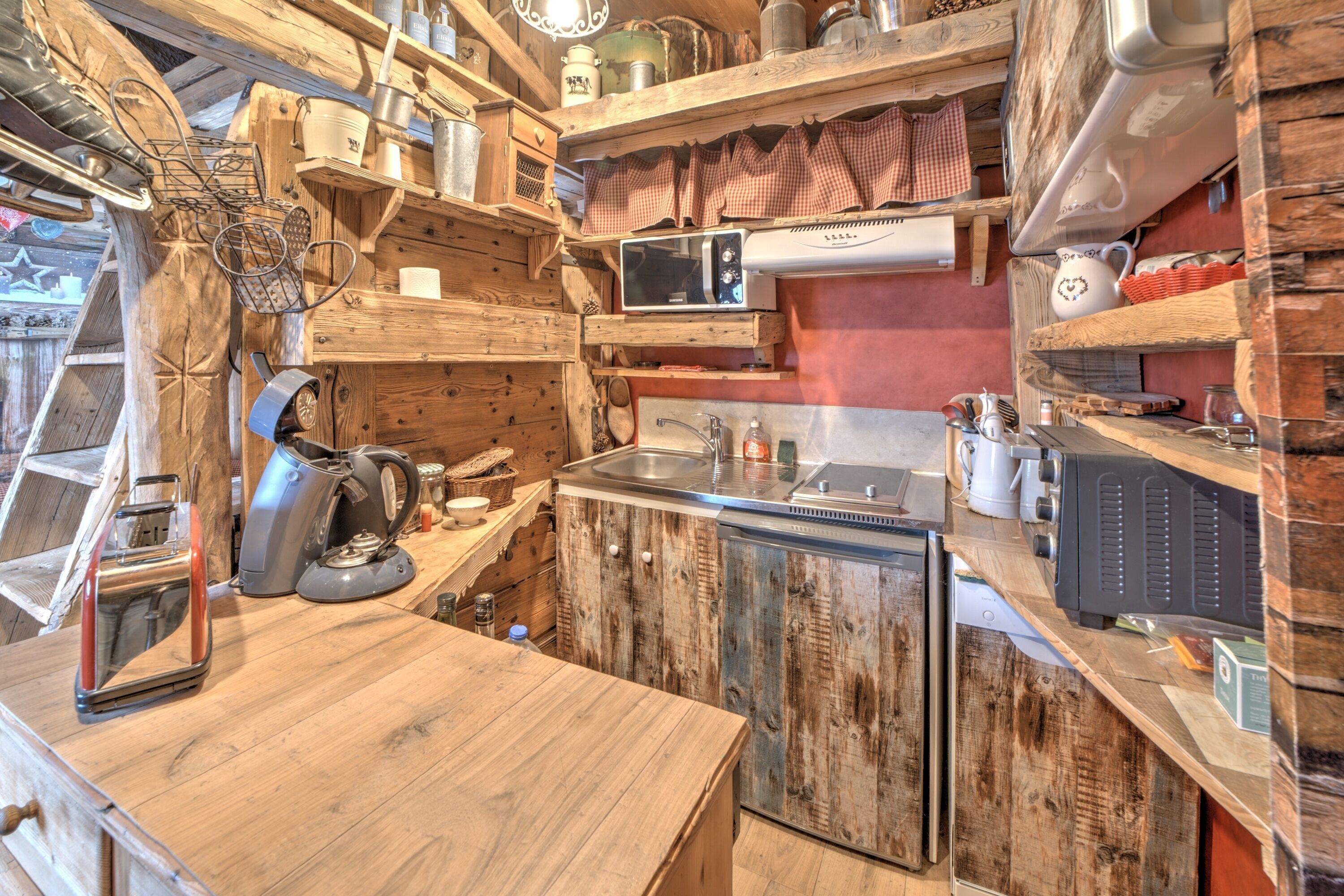 A rustic kitchen with wooden cabinets, a microwave, a kettle, and various kitchen utensils.