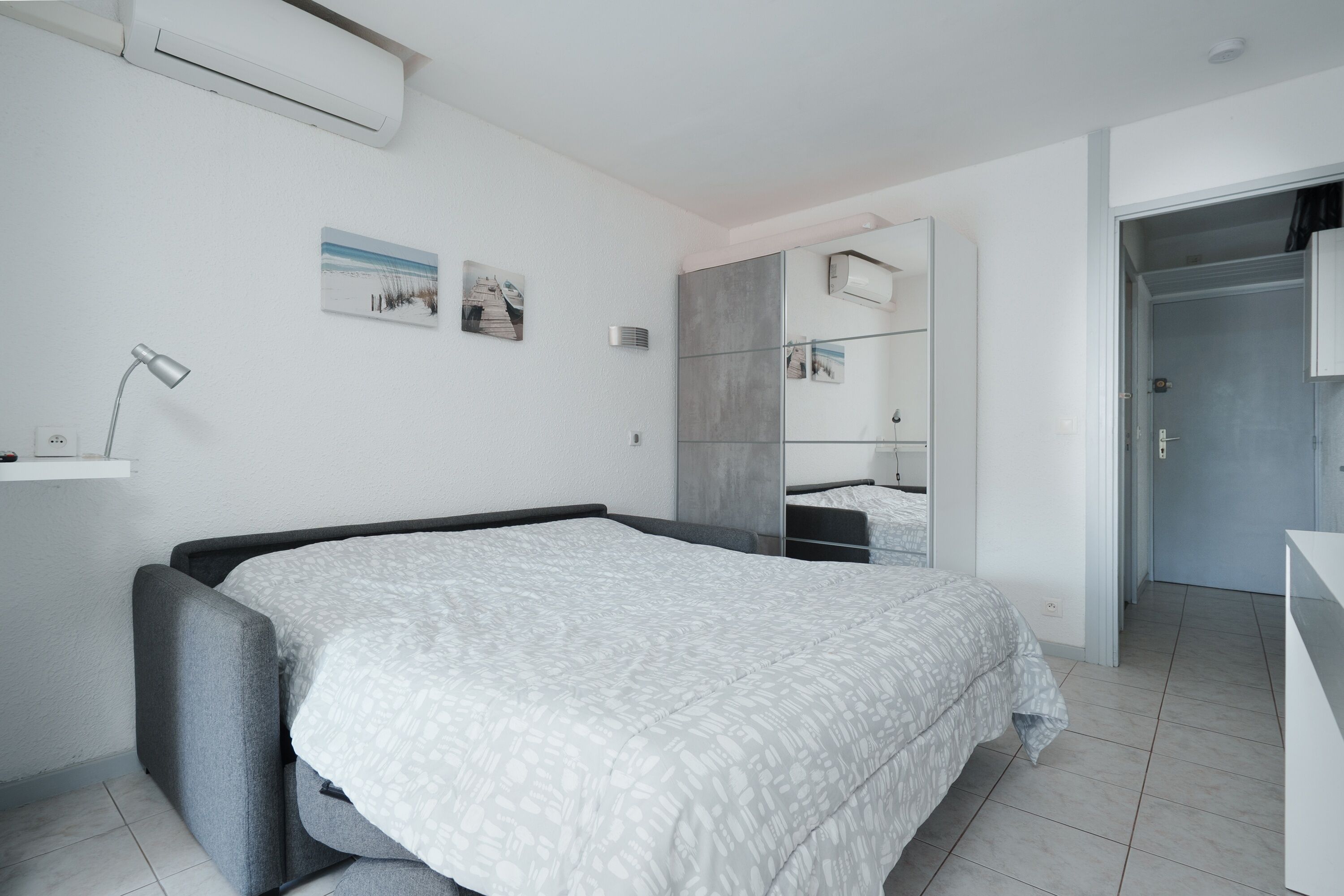 Quarto moderno com cama, mesa de cabeceira e ar condicionado na parede.