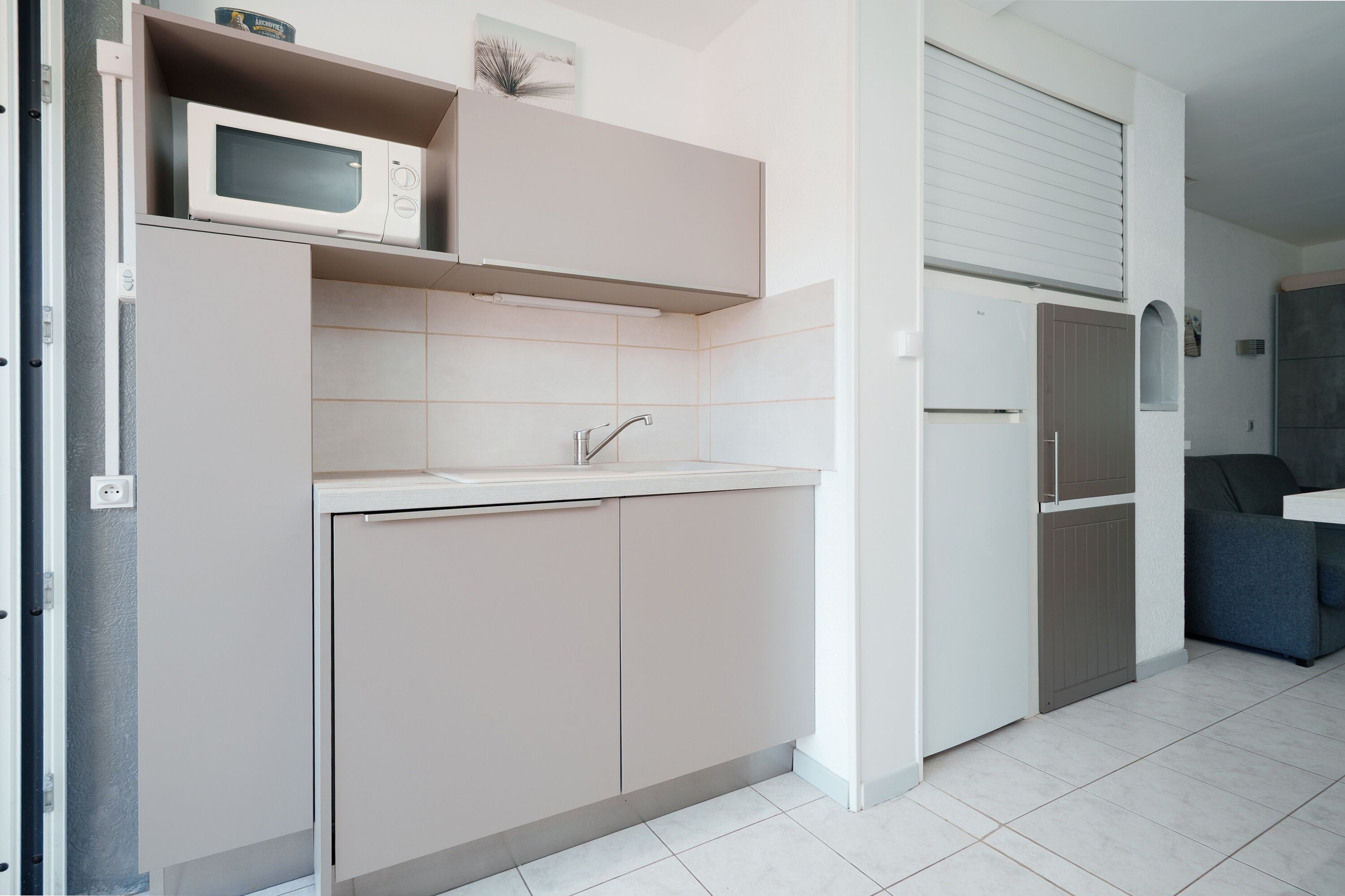 A compact kitchen with a microwave, sink, cabinets, and a refrigerator.