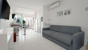 A modern living room with a grey sofa, a flat-screen TV mounted on the wall, and a kitchen area in the background. - Le Nid d'Agde - Climatisé, à quelques pas du port (Agde)
