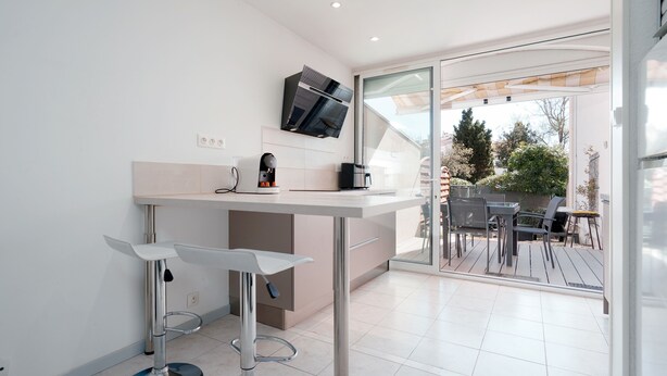 A modern kitchen with a built-in oven, a coffee machine, and a TV mounted above the counter. - Le Nid d'Agde - Climatisé, à quelques pas du port (Agde)