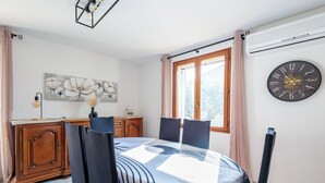 Una sala menjador amb una taula preparada per a quatre persones, un rellotge a la paret i una finestra amb cortines.