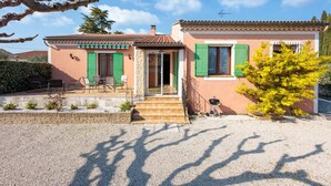 Una casa de dues plantes amb un patí, persianes verdes i un camí de grava.