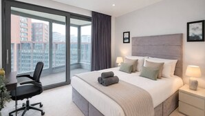 A hotel room with a large bed, a desk, a chair, and a view of the cityscape through the window. - Kings Cross Apt W/ Balconies | st pancras & camden (London)