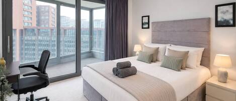 Habitación de hotel con una cama grande, un escritorio, una silla y vistas a la ciudad por la ventana.
