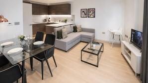 A modern living room with a sofa, a dining table set for four, a coffee table, and a television. - Kings Cross Apt W/ Balconies | st pancras & camden (London)