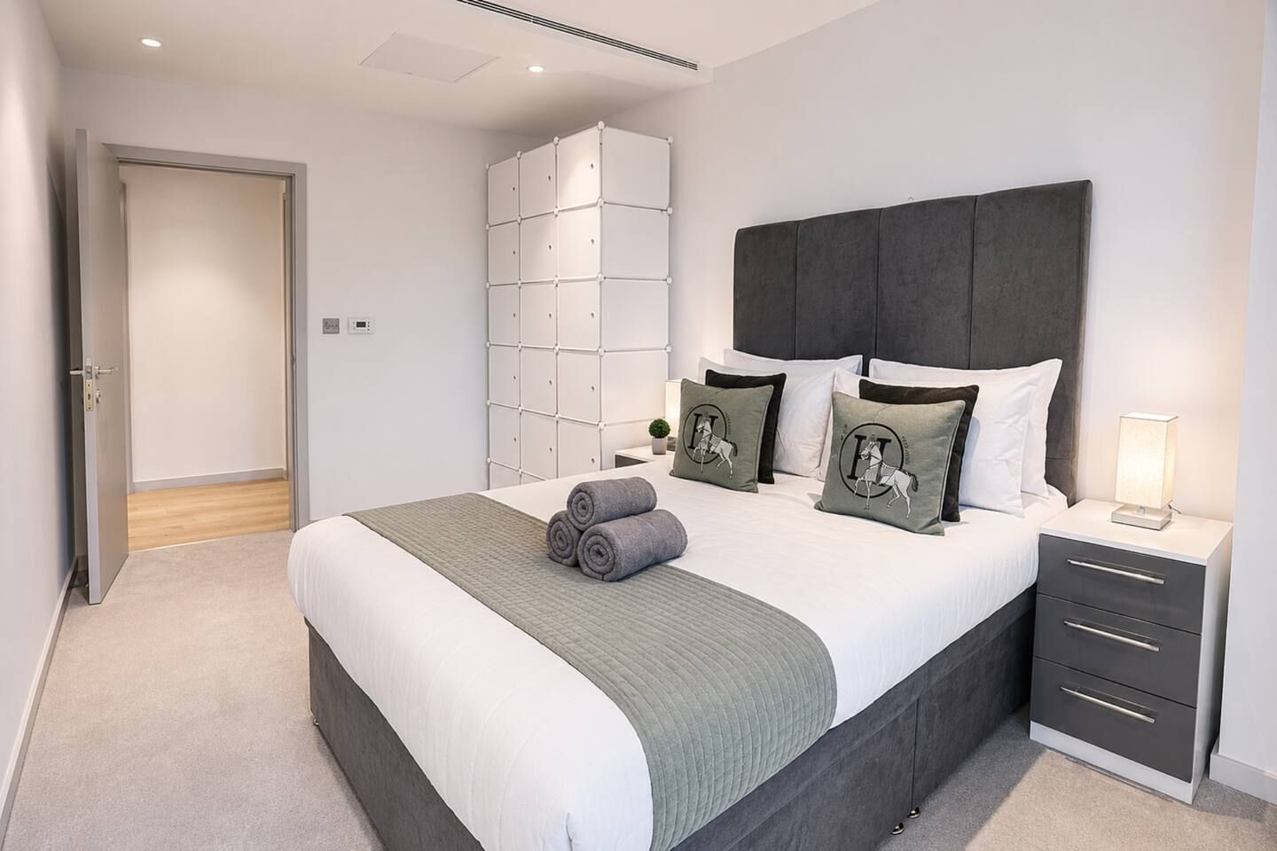 Un dormitorio con cama, mesitas de noche, un armario y una puerta que da a otra habitación.