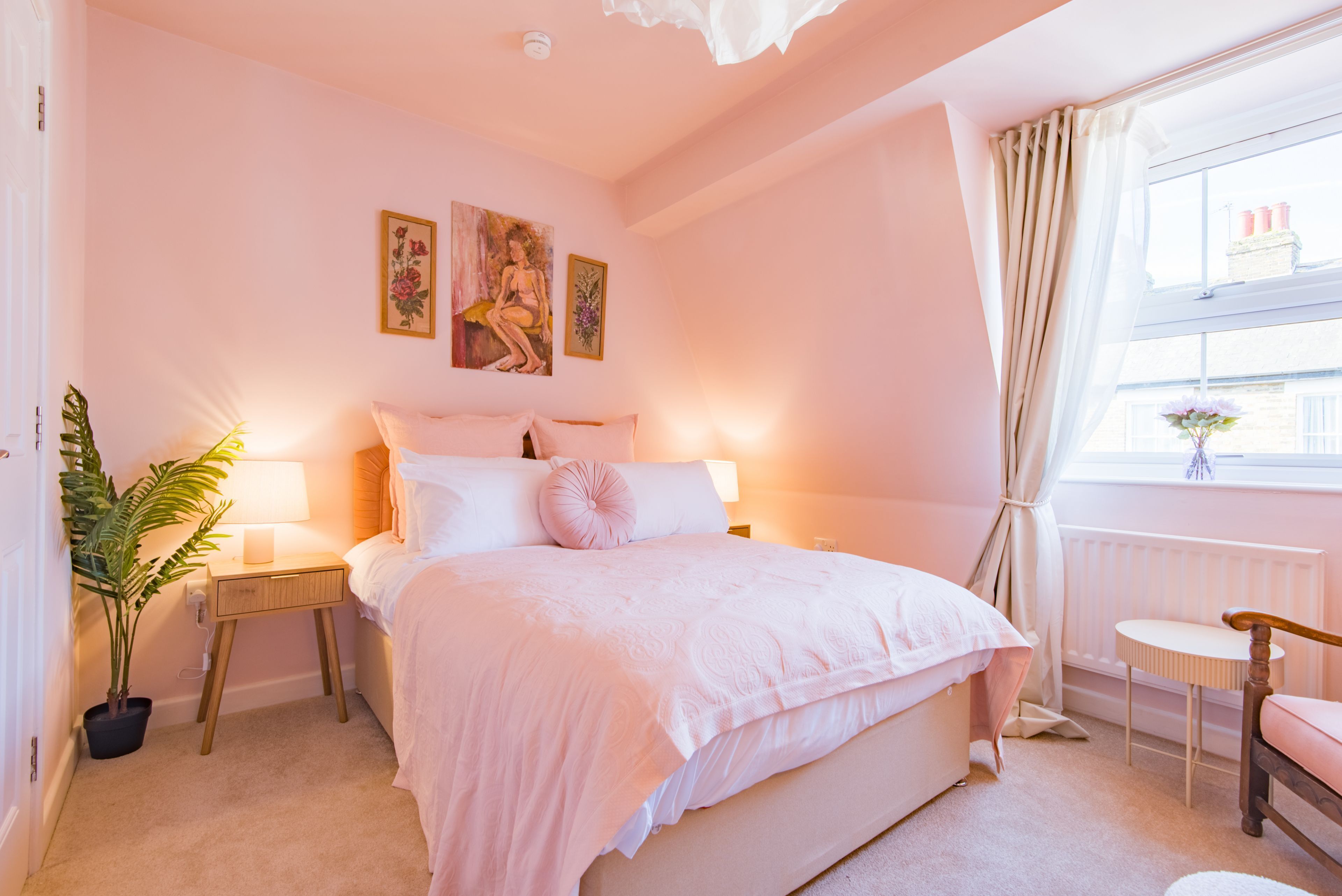 A bedroom with a bed, bedside tables, a potted plant, and artwork on the wall.