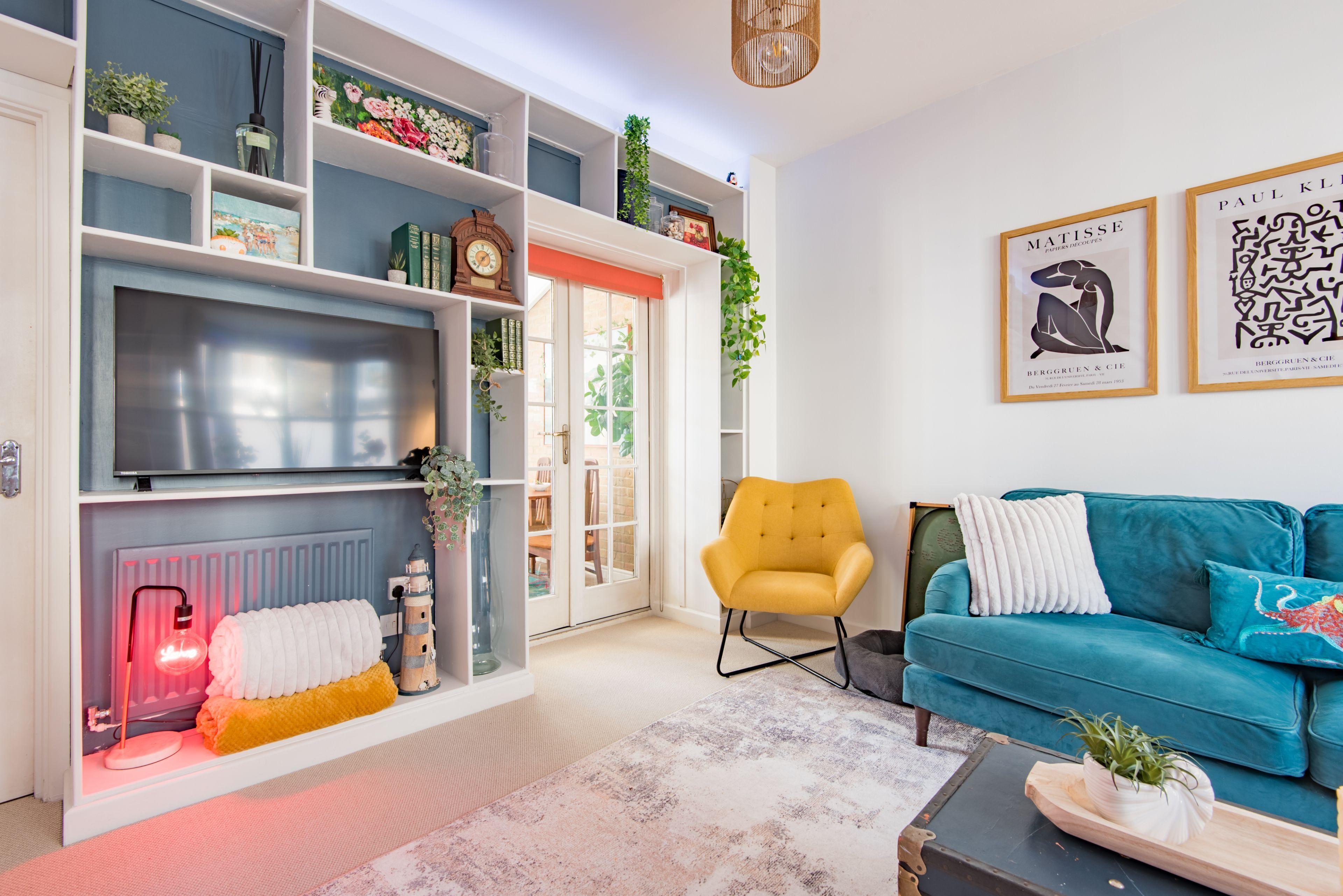 Ein Wohnzimmer mit Fernseher, einem gelben Sessel, einem blaugrünen Sofa und einem Kamin.