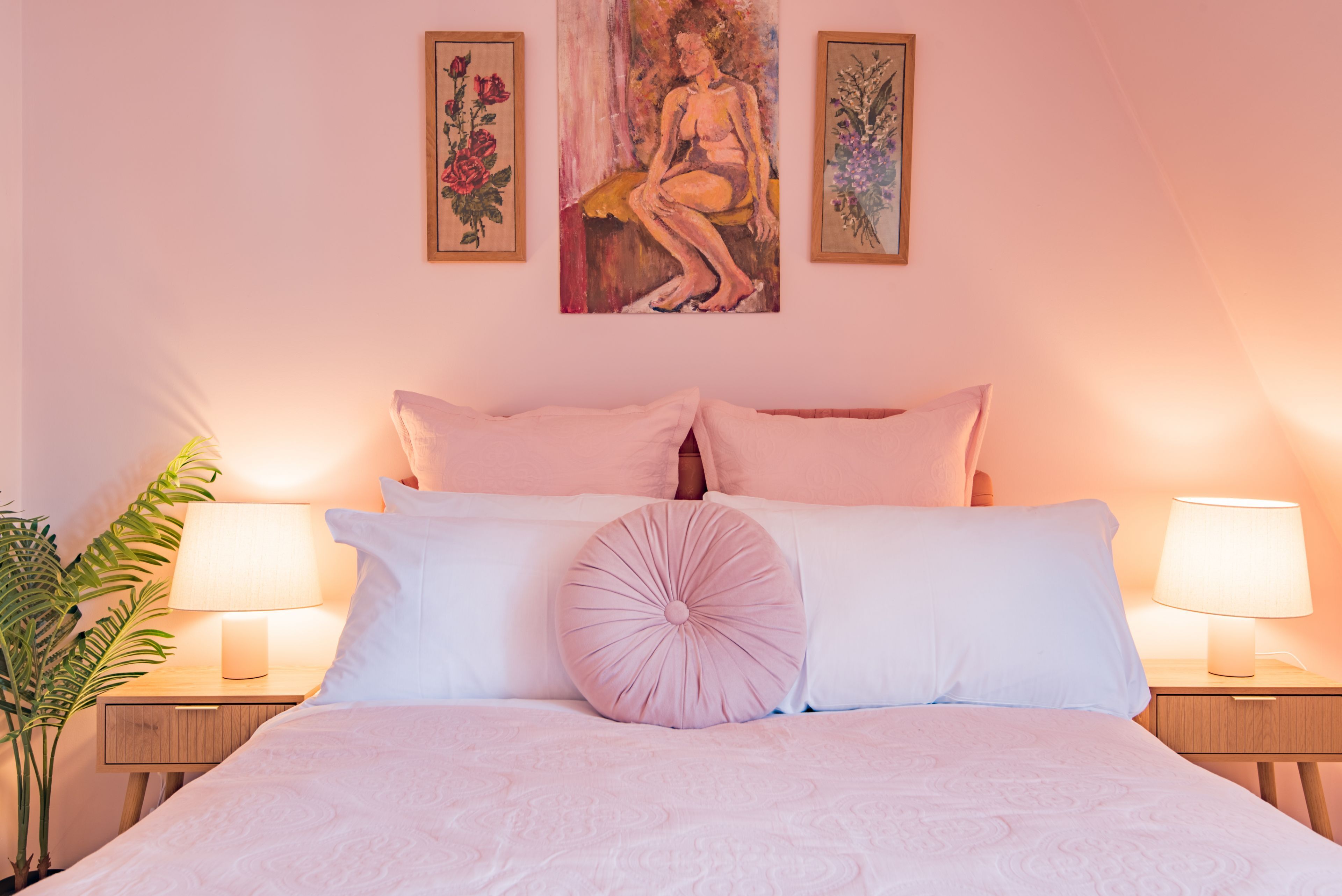 Une chambre à coucher avec un lit, deux lampes de chevet, une plante en pot et des œuvres d’art accrochées au mur.