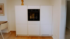 Una cocina compacta con horno integrado, un armario blanco y una escultura de madera encima.