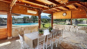 A wooden interior with a stone floor, a table with chairs, and a view of a swimming pool and greenery outside. - Villa Aresini – Exclusive Residence (Montemiletto)