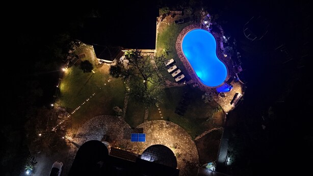 An aerial view of a property with a swimming pool, stone pathways, and outdoor lighting. - Villa Aresini – Exclusive Residence (Montemiletto)