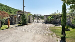 A gated entrance with a stone wall, a house in the background, and a clear sky. - Villa Aresini – Exclusive Residence (Montemiletto)
