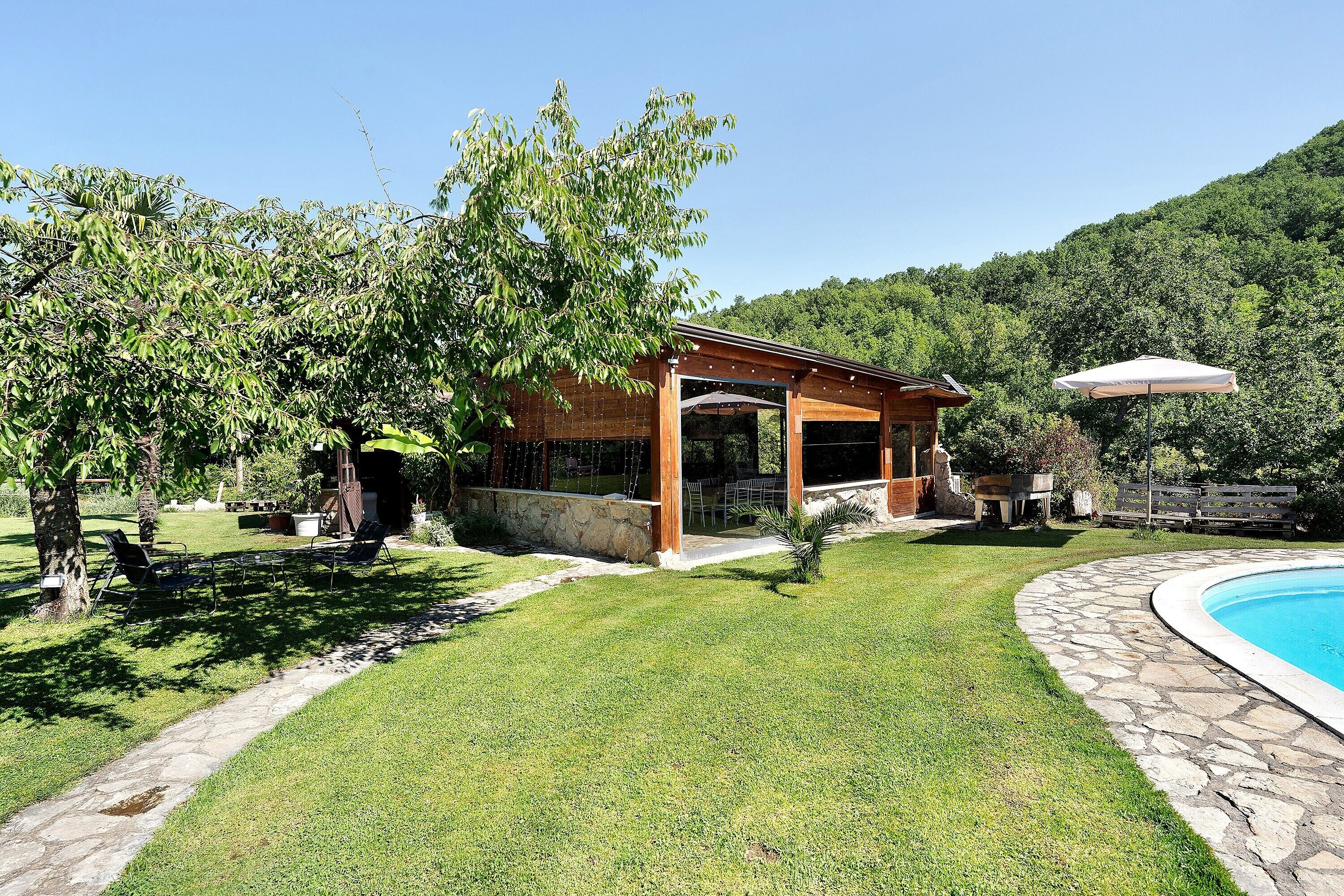 A poolside area with a stone pathway, a small building with an open door, and a tree.