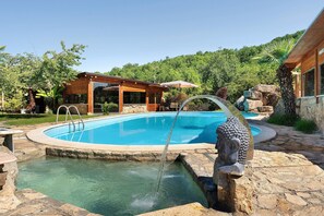 Une piscine agrémentée d’une cascade, entourée d’escaliers en pierre et d’une terrasse en bois.