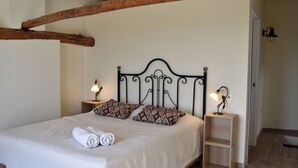 Ein Bett mit weißer Bettdecke, zwei Kissen und zusammengerollten Handtüchern. Zwei Nachttische mit Lampen stehen daneben.