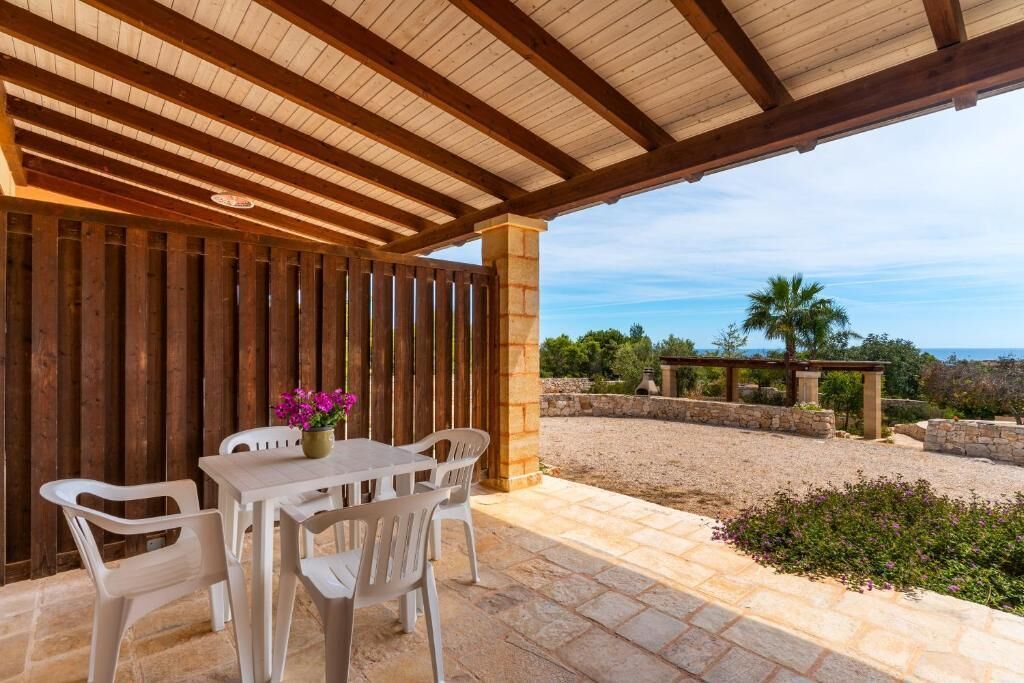 Eine überdachte Terrasse mit Tisch und Stühlen, ein Holzzaun und eine Landschaftsaussicht.
