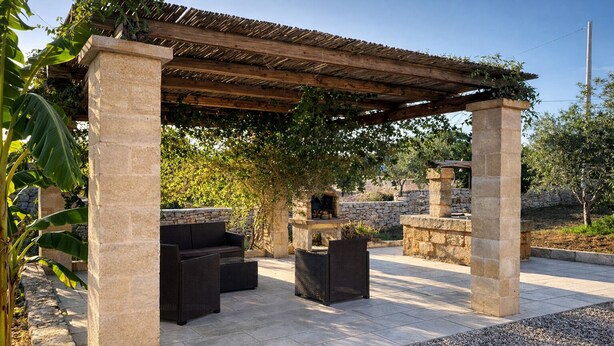 Eine Außenpatio mit Steinpfeilern, einer Pergola, Korbmöbeln und einem Steinkamin.