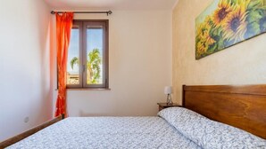 Ein Schlafzimmer mit Bett, Vorhängen an einem Fenster, einem Nachttisch und einem Bild an der Wand.