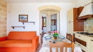 Zona pranzo con tavolo imbandito per due, divano e cucina completa di pensili e fornello.