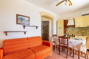 A room with a sofa, a dining table with chairs, a kitchen area with cabinets, and a ceiling fan. - Residence with pool - Suite Lavender (Torre Pali)