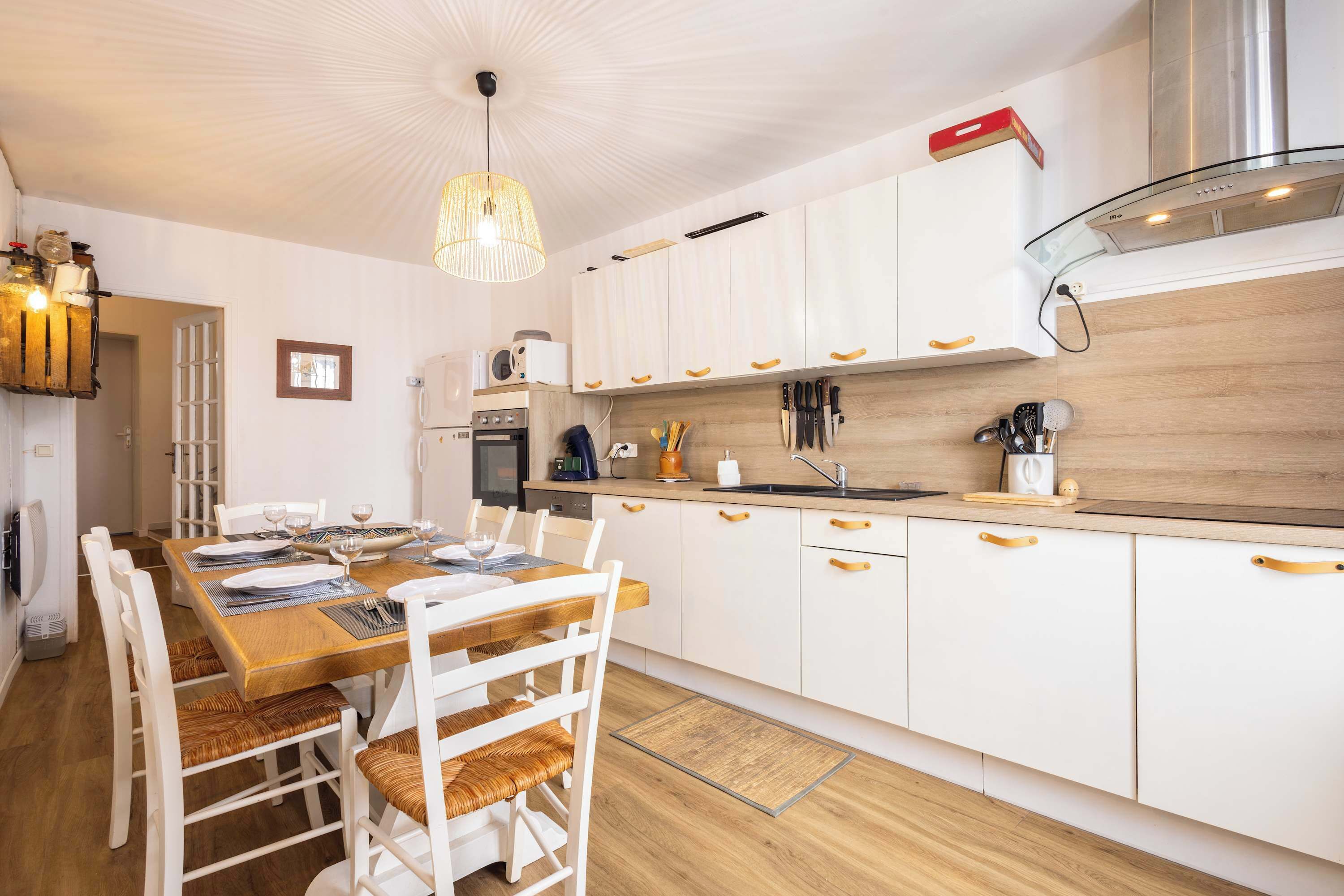 A modern kitchen with white cabinets, a wooden dining table, and a hanging light fixture.
