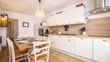 A modern kitchen with white cabinets, a wooden dining table, and a hanging light fixture.